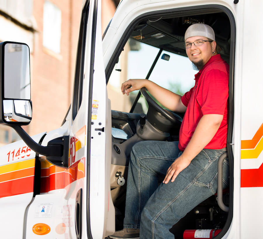 Man with red shirt sitting in an RTS truck cab with the door open smiling