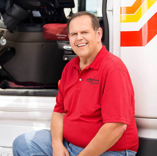 RTS truck driver with red shirt smiling sitting in front of the open door of a truck cab